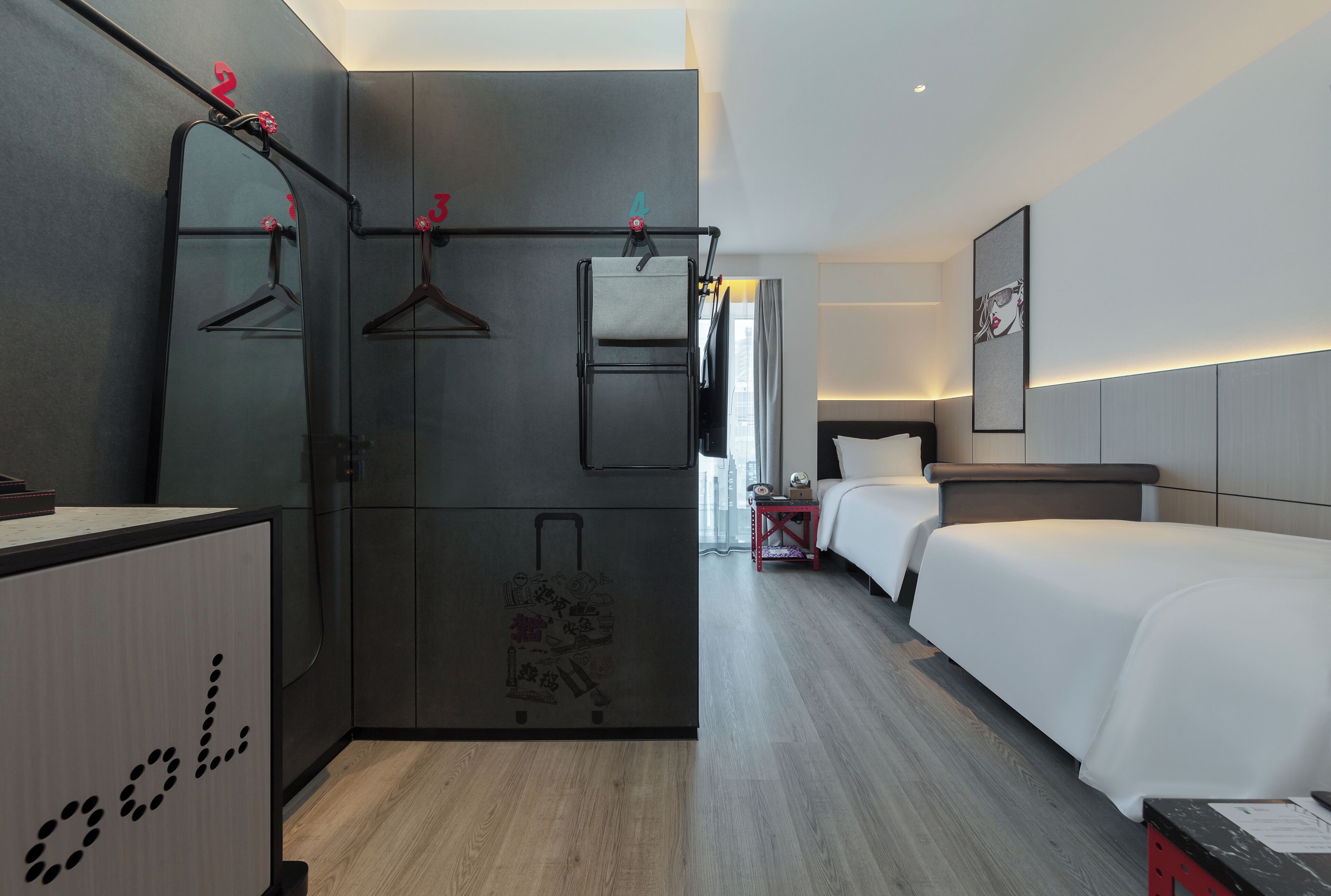 A hotel room with a wardrobe, a bed, a bedside table, and a mirror.
