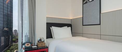 A modern hotel room with a large bed, a small bedside table with a telephone, and a city view through the window.