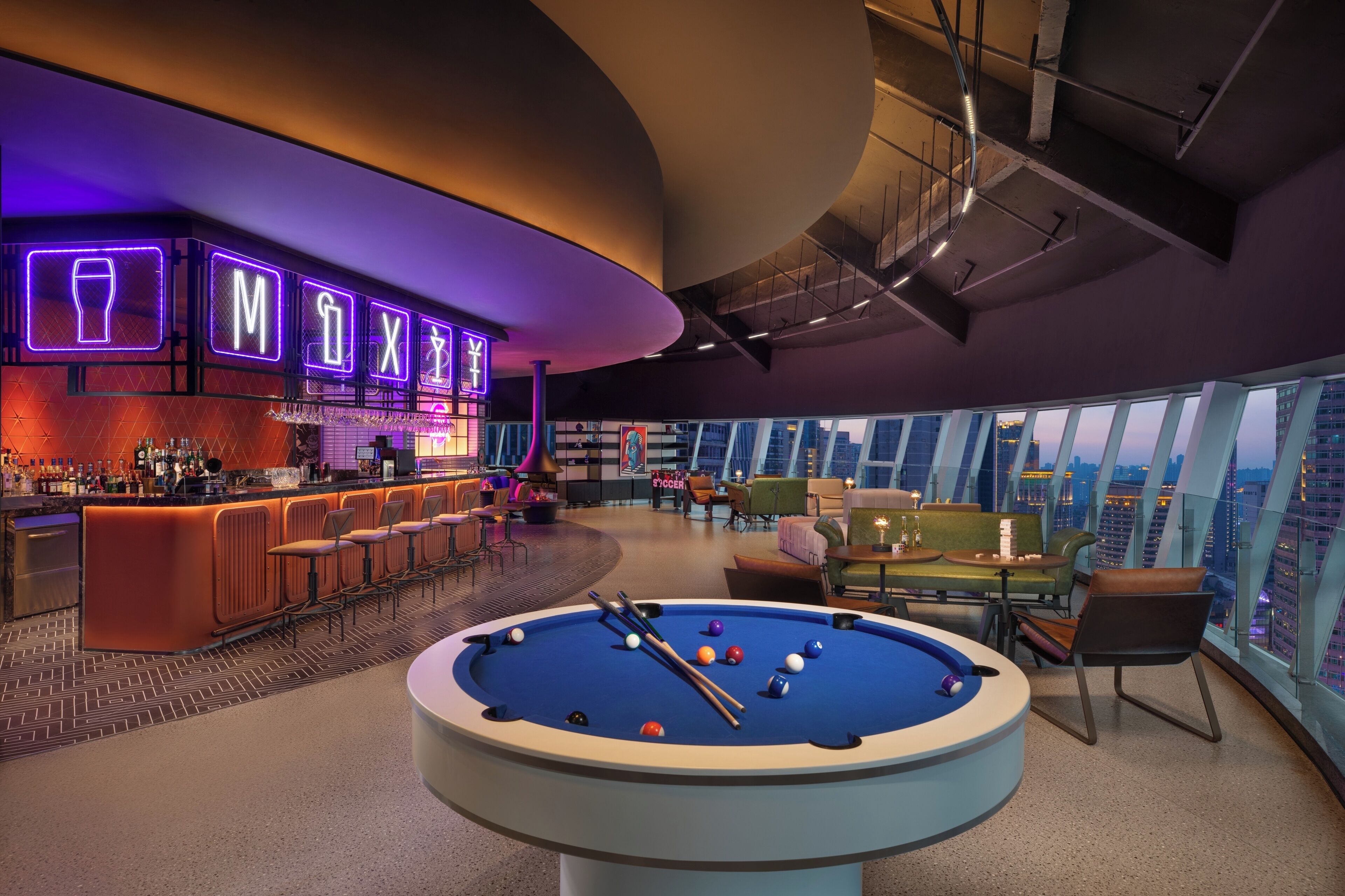 Un espace bar moderne, agrémenté d’enseignes au néon, d’une table de billard et offrant une vue sur la ville.