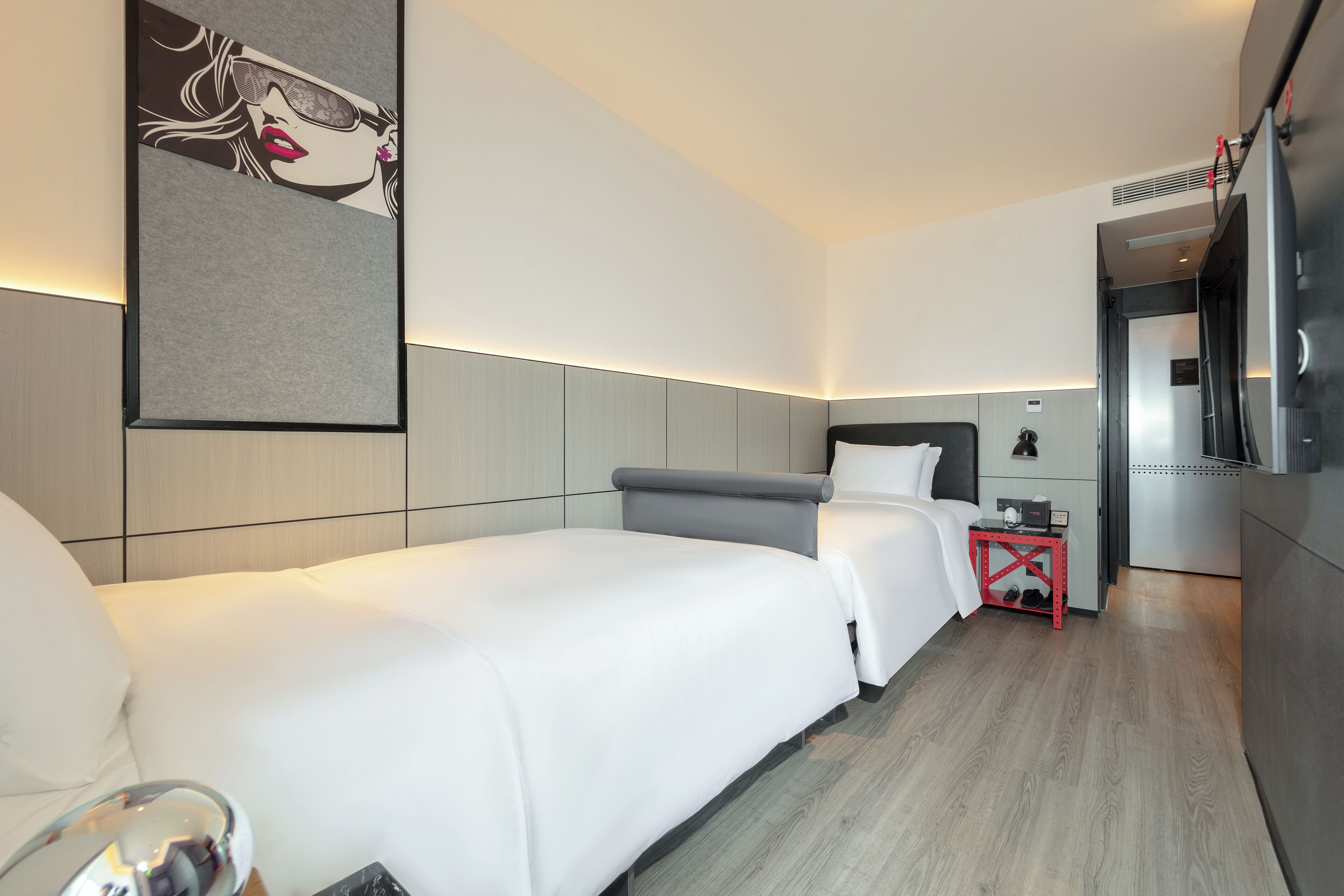 Quarto de hotel com duas camas, uma mesinha, televisão e frigorífico.