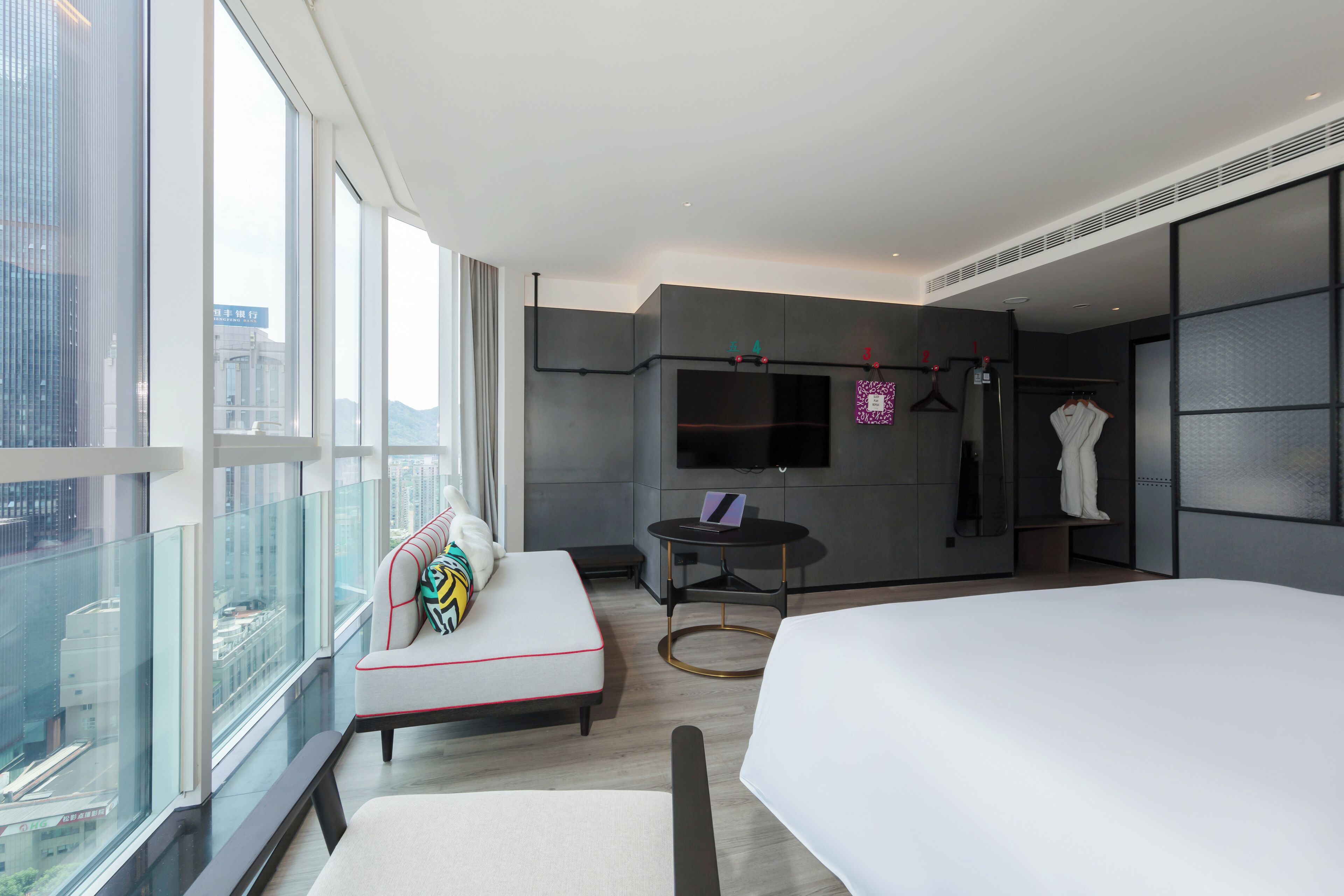 Une chambre d’hôtel moderne avec un grand lit, un canapé, une télévision et une vue sur la ville.