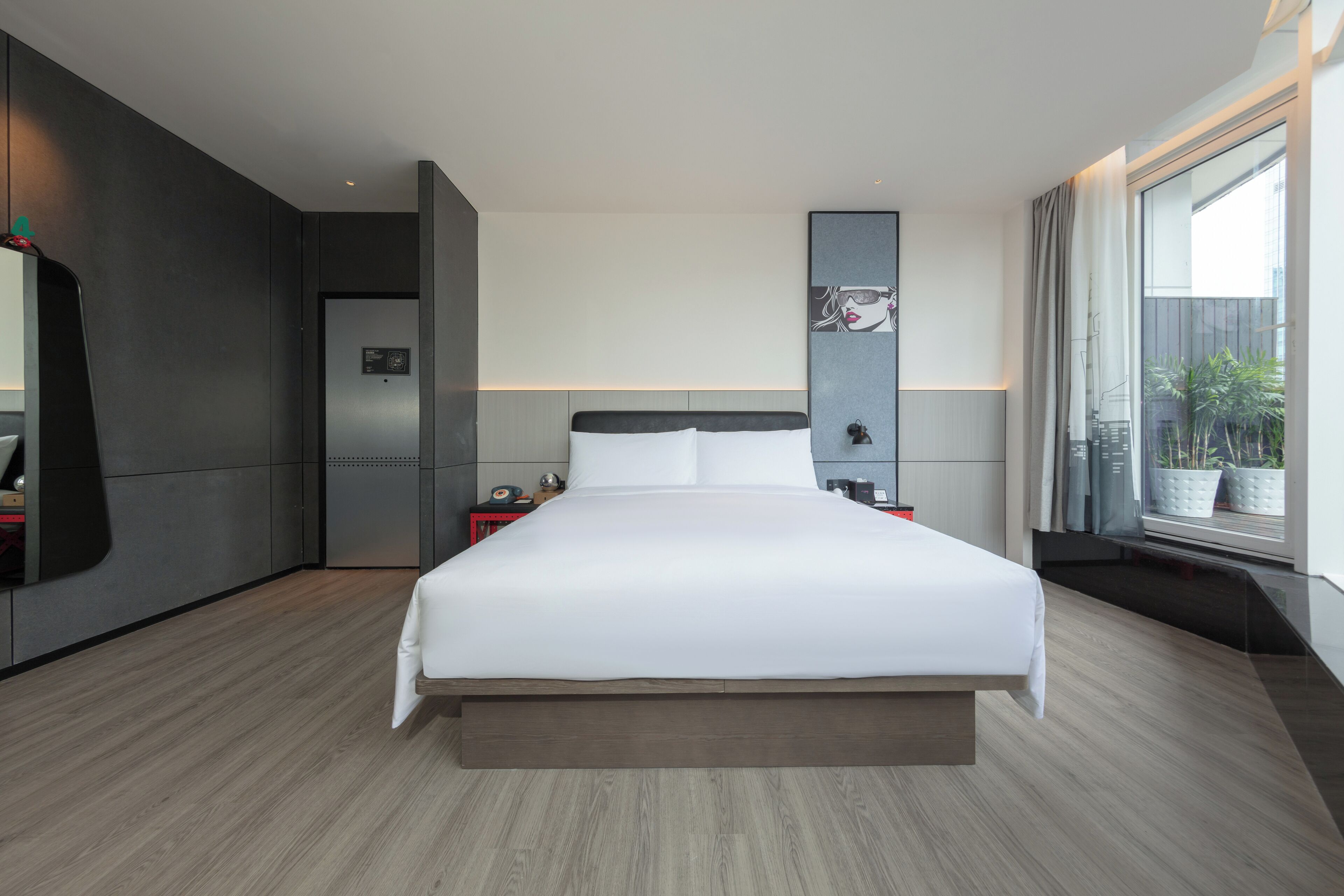 Quarto de hotel moderno com uma cama grande, um guarda-roupa embutido, uma pequena mesa de cabeceira e uma janela ampla com vista para o exterior.