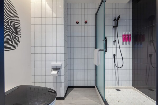 A modern bathroom with a glass shower enclosure, white tiled walls, a black bathtub, and a toilet paper holder.