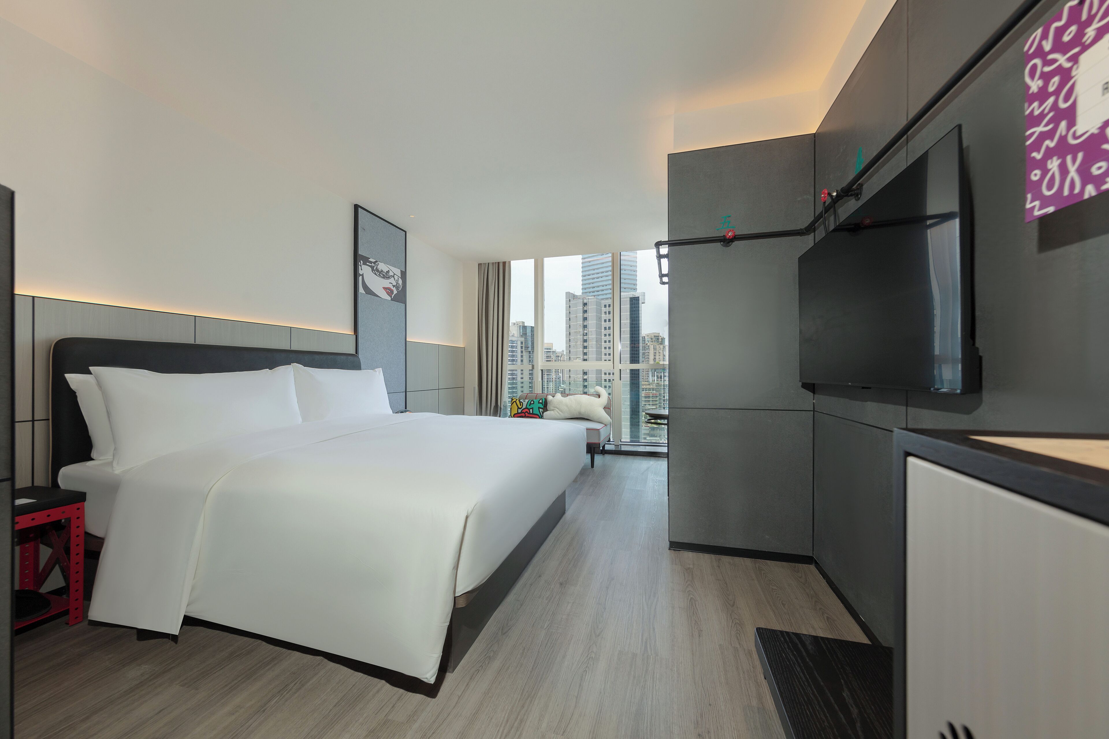 Une chambre d’hôtel moderne avec un grand lit, un téléviseur fixé au mur et une vue sur la ville par la fenêtre.