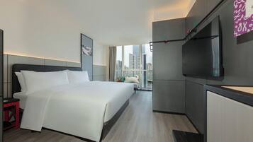 Une chambre d’hôtel moderne avec un grand lit, un téléviseur fixé au mur et une vue sur la ville par la fenêtre.