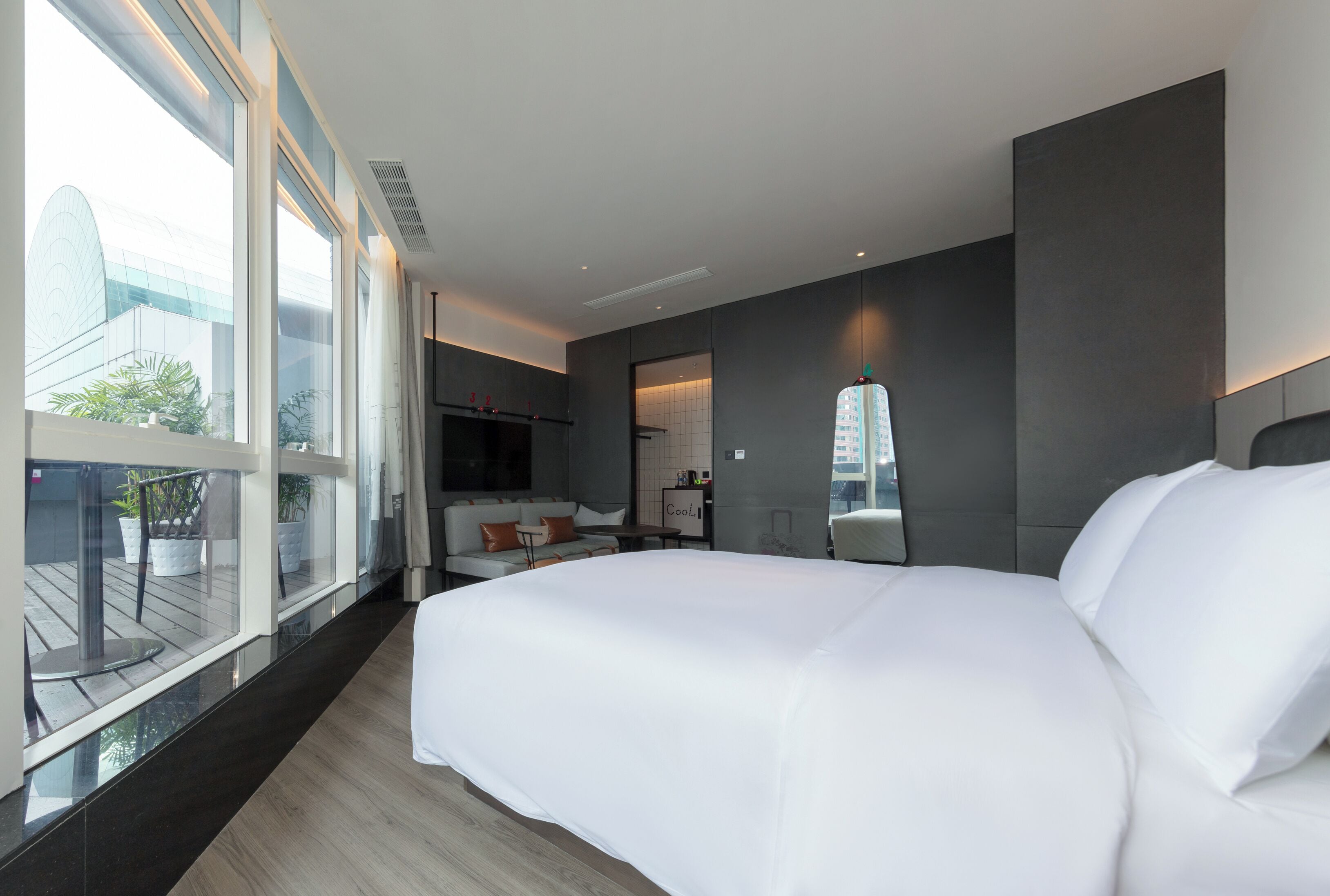 A modern hotel room with a large bed, a small seating area, a large window, and a view of the city.