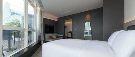 A modern hotel room with a large bed, a small seating area, a large window, and a view of the city.