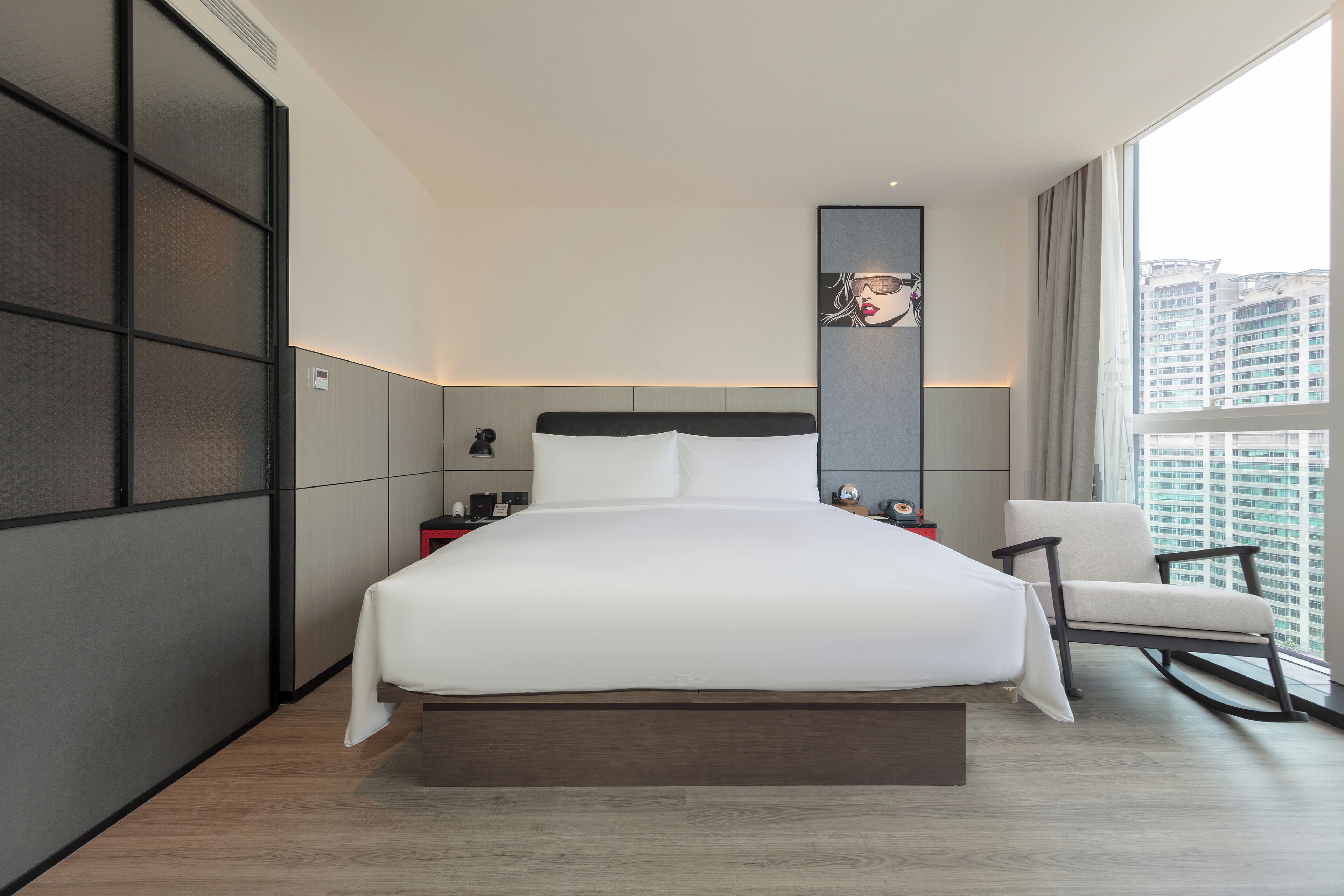 Une chambre d’hôtel moderne avec un grand lit, une chaise, une table de chevet et une vue sur la ville.