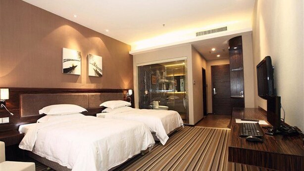 A hotel room with two beds, a desk with a computer, a TV, and a glass shower area. - Zhuhai Harmony Resort Hotel (Zhuhai)