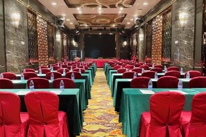 Un salón de conferencias con filas de mesas y sillas, un escenario y piso alfombrado.