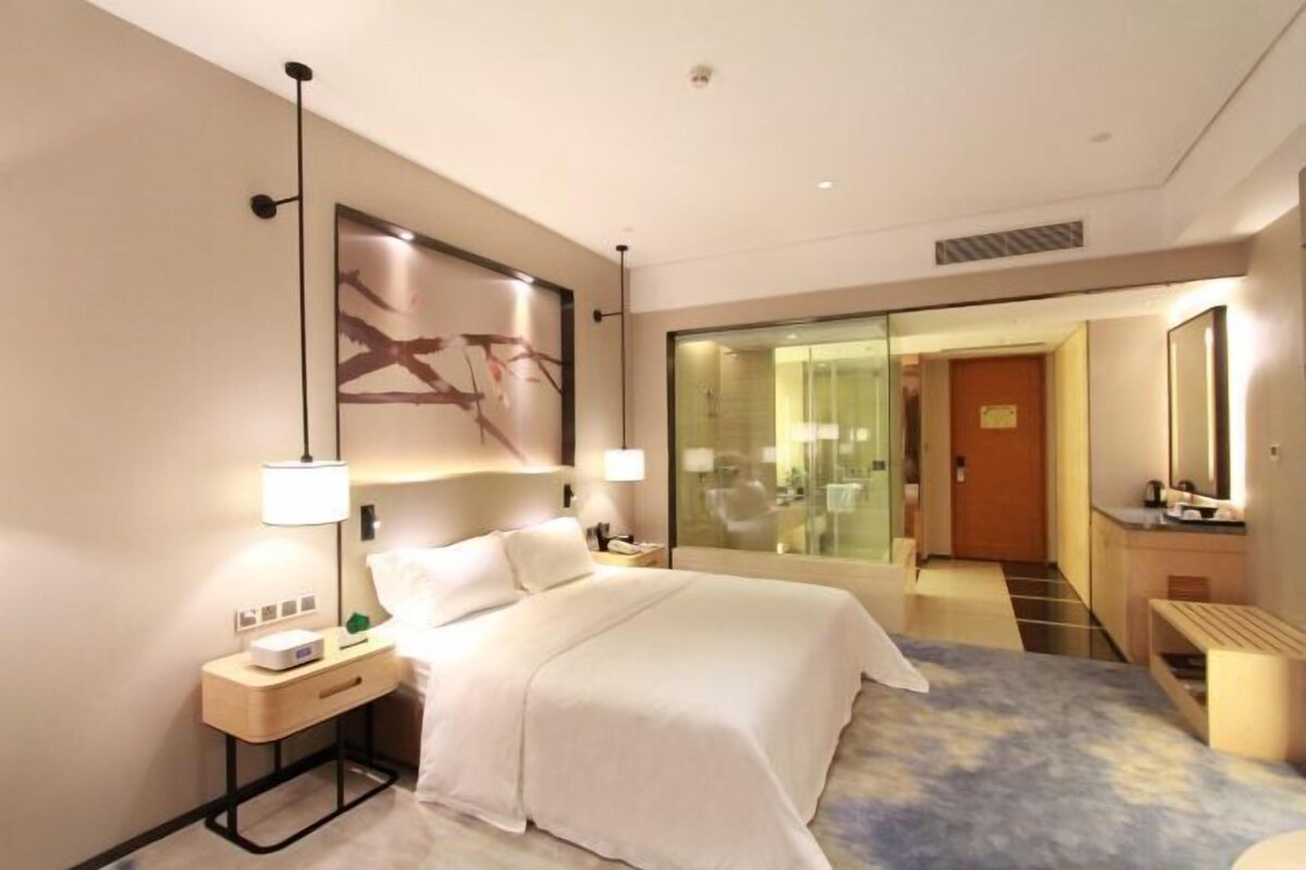 Ein modernes Hotelzimmer mit Bett, Nachttisch, Lampe und einem großen Spiegel.