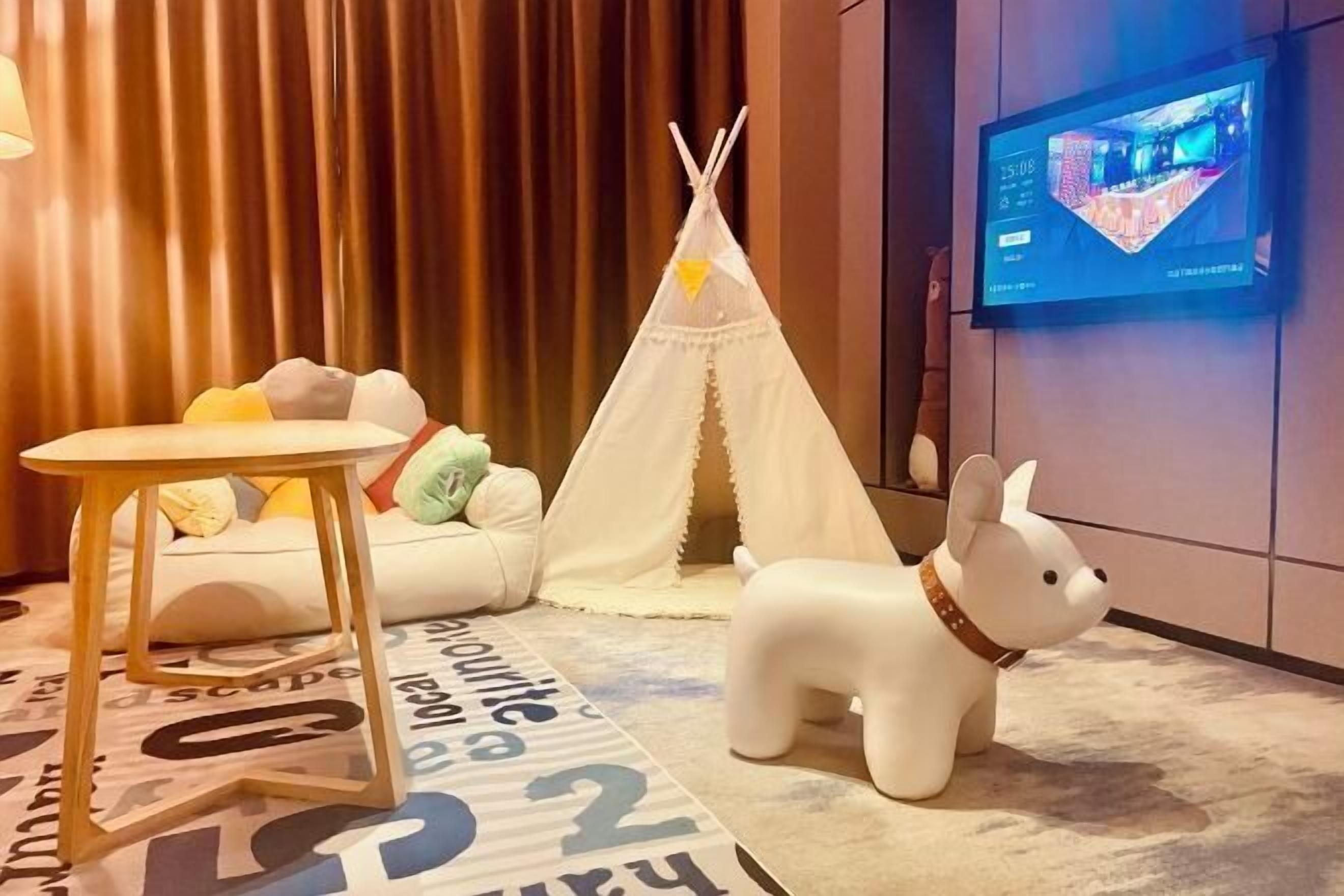 Una habitación acogedora con un sofá blanco, una mesita de madera, una figurita de perro blanco, un tipi blanco y un televisor montado en la pared.