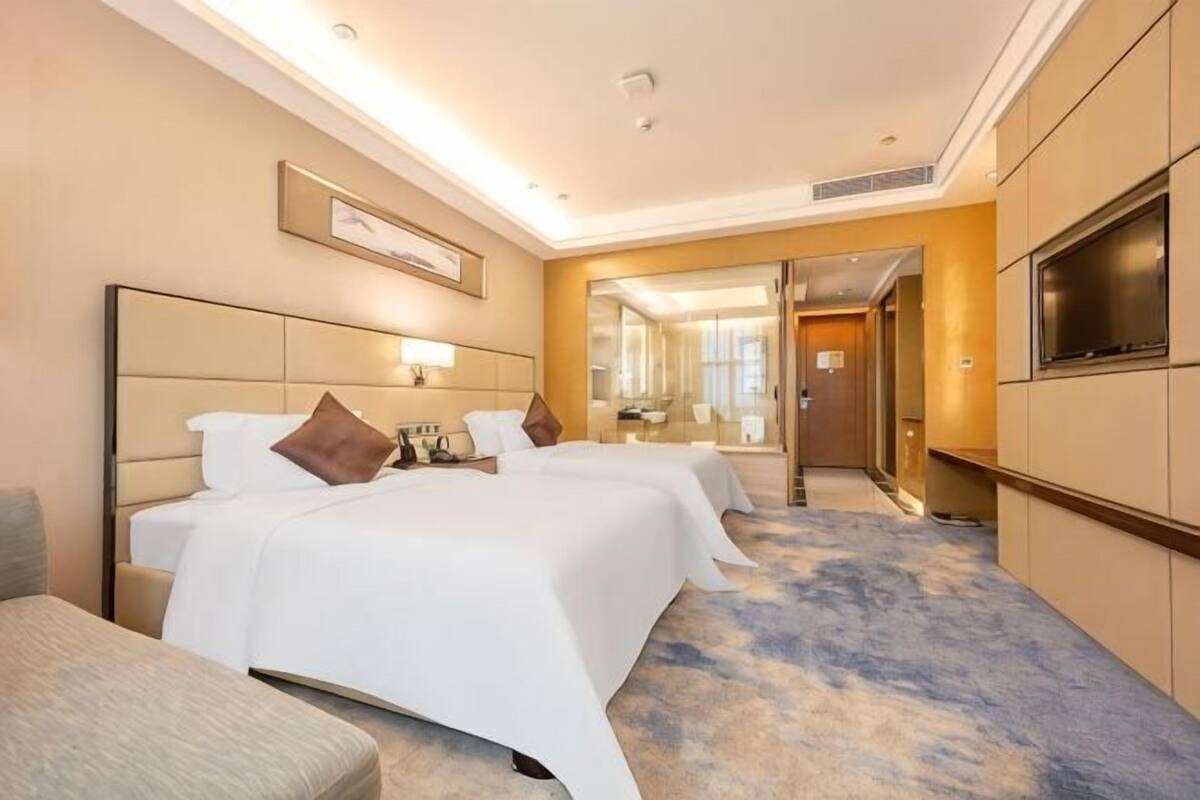 A hotel room with two beds, a TV, a sofa, and a large mirror.