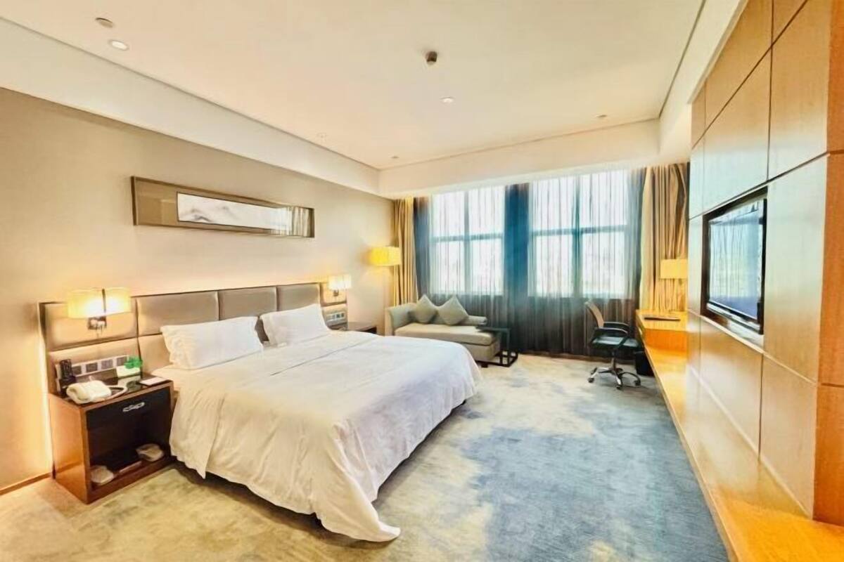 A hotel room with a large bed, bedside tables, a desk, and a window with curtains.