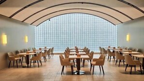 Un salón de conferencias con varias mesas y sillas, ventanas amplias y un techo curvo.