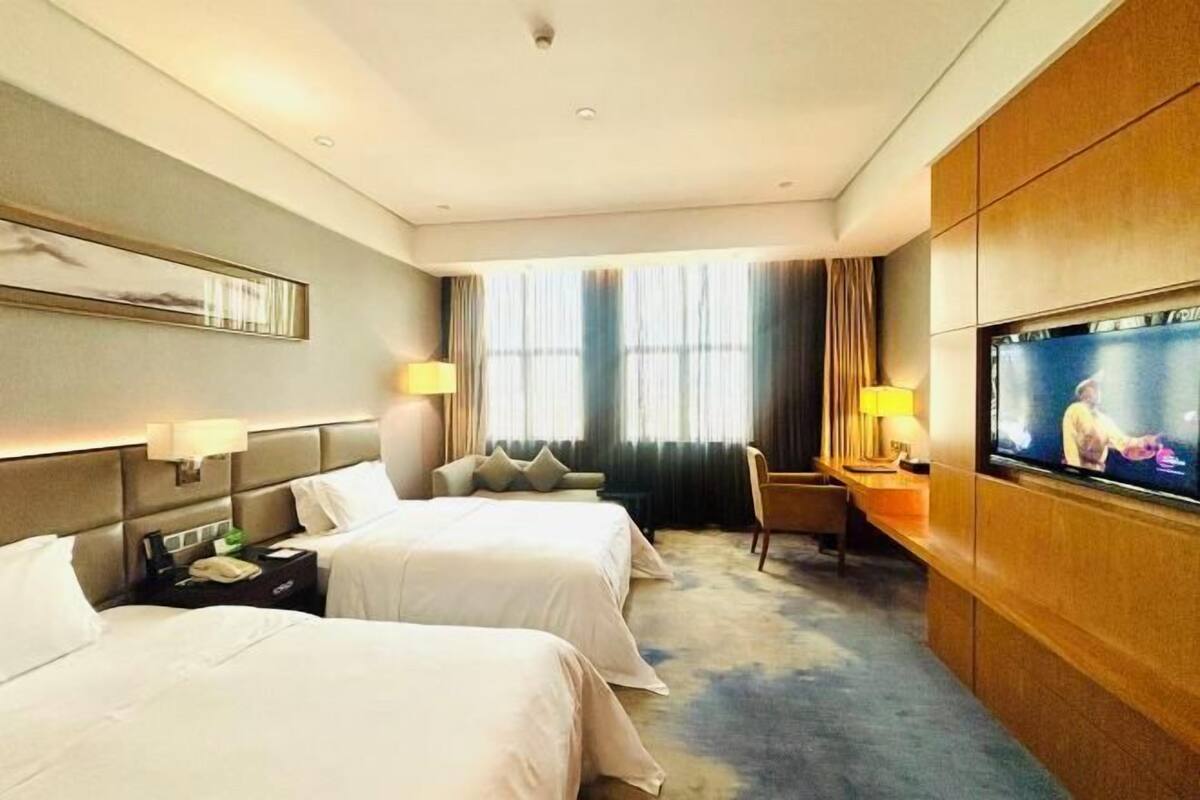 A hotel room with two beds, a television, a desk with a lamp, and a window with curtains.