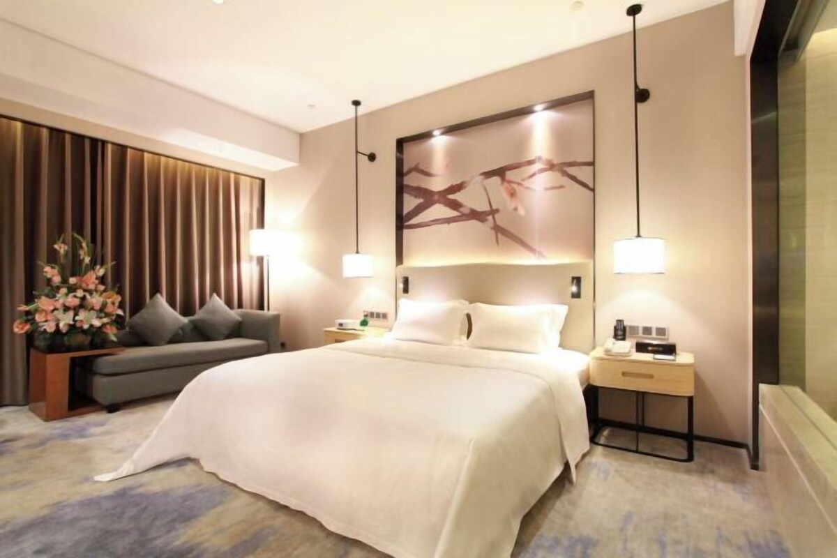 Ein modernes Hotelzimmer mit einem großen Bett, einer Couch, einem Nachttisch und einem Wandbild.