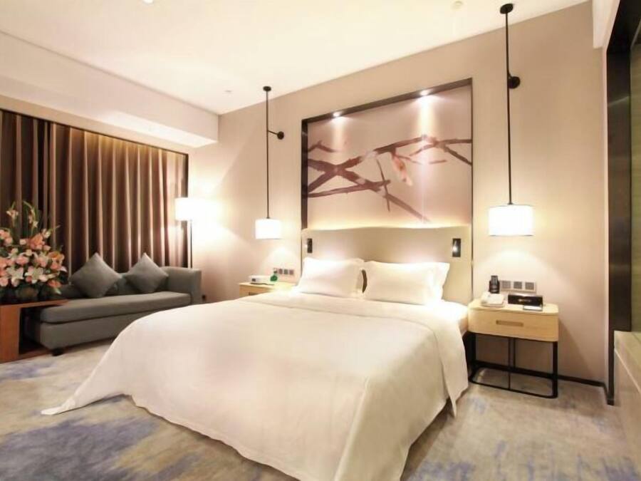 Une chambre d’hôtel moderne avec un grand lit, un canapé, une table de chevet et une œuvre d’art accrochée au mur.