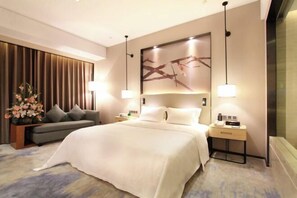 A modern hotel room with a large bed, a sofa, a nightstand, and a wall-mounted artwork. - Shuidu Holiday Hotel Shenzhen (Shenzhen)