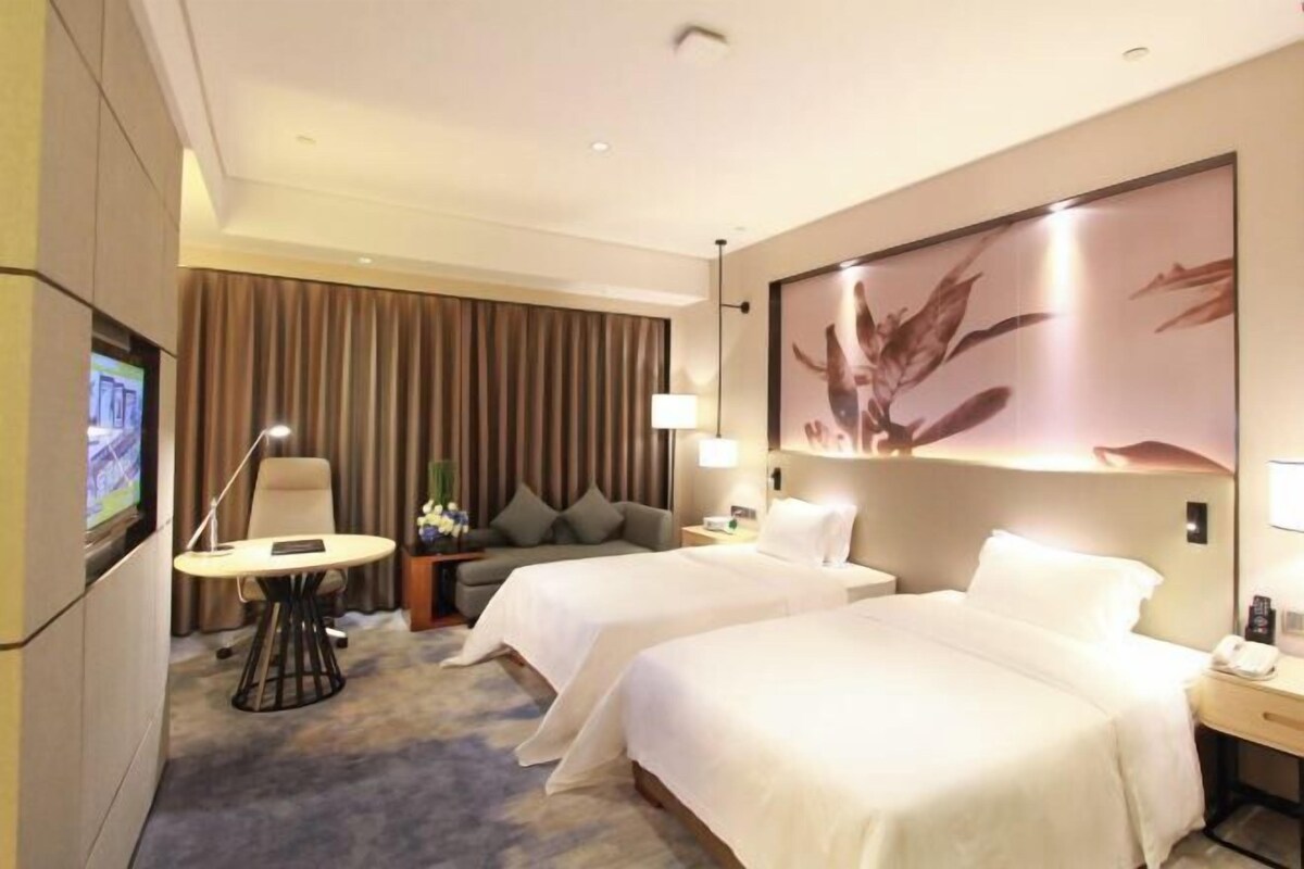 Ein Hotelzimmer mit zwei Betten, einem Schreibtisch, einem Stuhl, einem Fernseher und einem großen Blumenbild an der Wand.