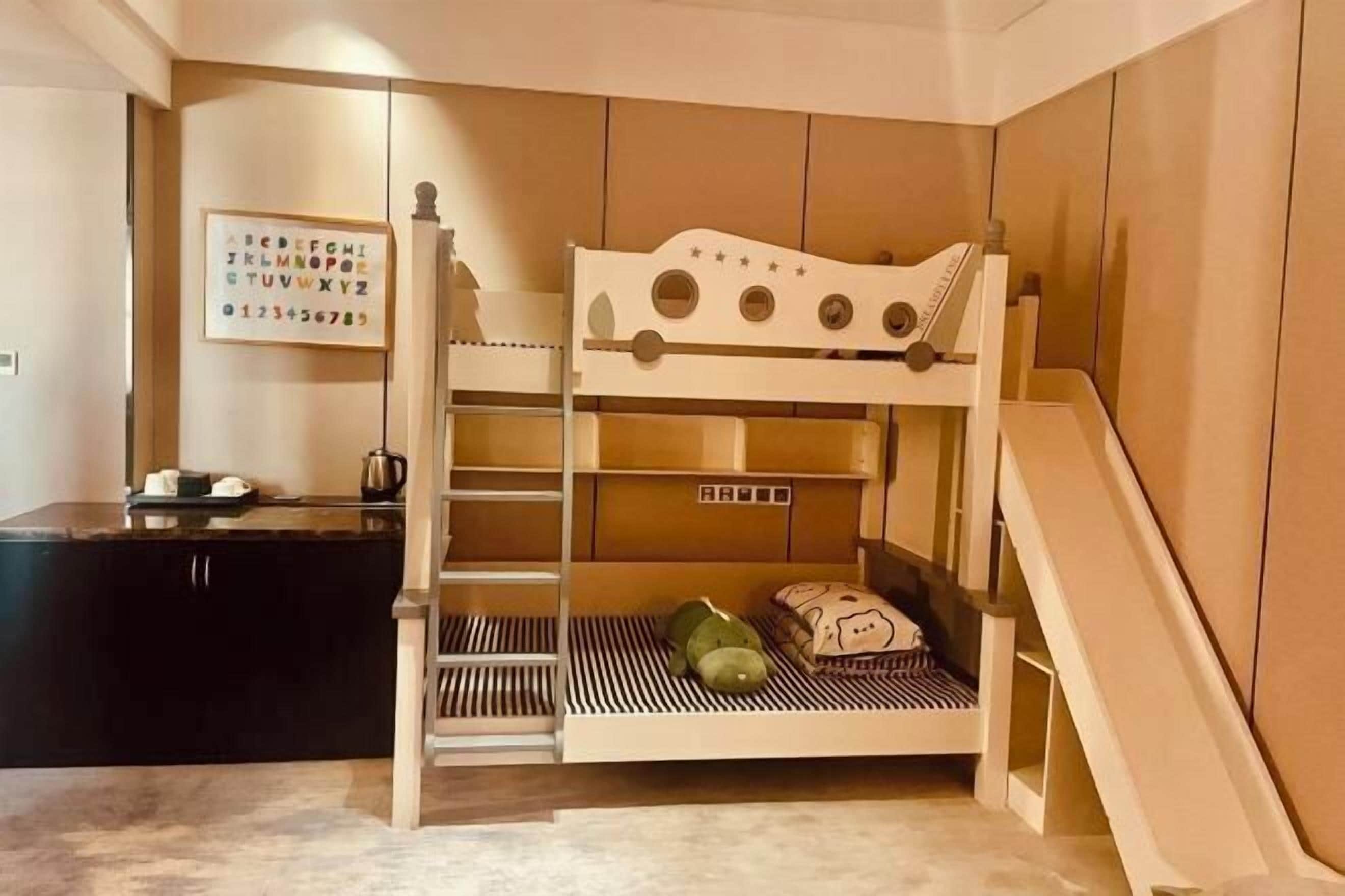 Una cama litera con escritorio y silla, una pequeña escalera y una pared con un cartel del alfabeto enmarcado.
