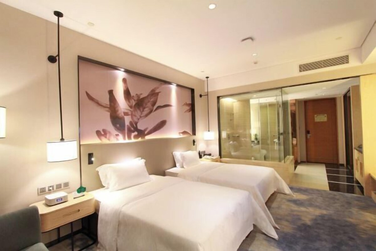 Ein Hotelzimmer mit zwei Betten, einem Schreibtisch, einer Lampe und einem großen Blumenbild an der Wand.