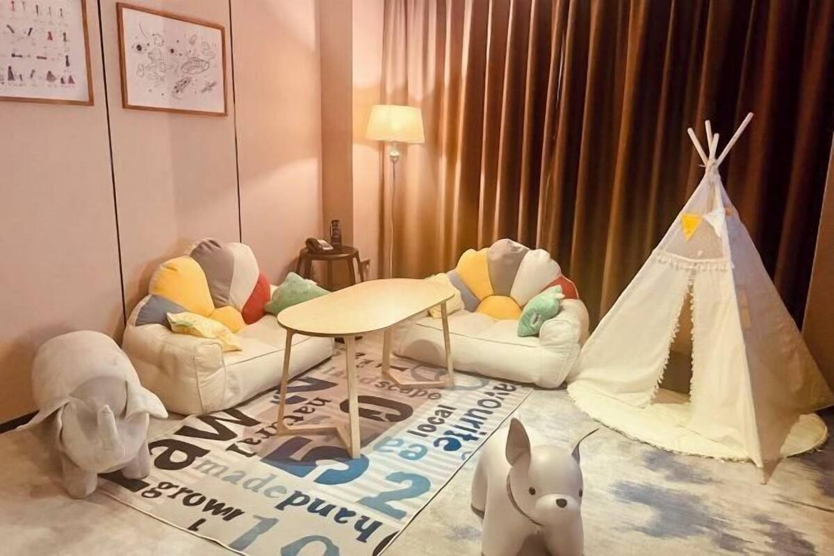 A cozy room with a sofa, a small table, a lamp, a teepee, and two elephant-shaped cushions.
