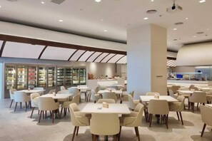 Un espacio interior amplio con varias mesas y sillas, un pilar grande y una vista de un mostrador refrigerado al fondo.