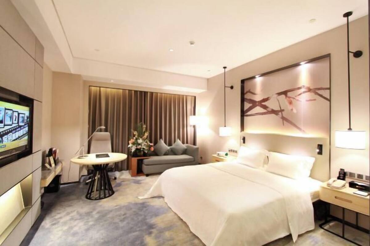 A hotel room with a bed, a TV, a desk, a chair, and a lamp.