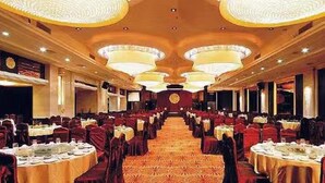 Une salle de banquet avec des tables rondes, des chaises rouges et des lustres.