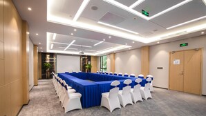 Una sala de conferències amb una taula llarga, cadires blanques i un mantell blau.