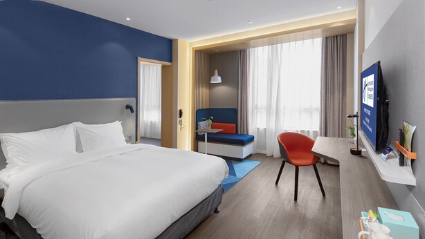 Habitació d'hotel amb un llit gran, una taula de treball, una cadira, televisió i una finestra amb cortines.