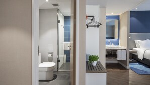 Un bany modern amb vàter, dutxa i un lavabo. Hi ha una planta sobre una prestatgeria i un penjador de tovalloles a la paret.