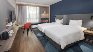 Una habitació d'hotel amb un llit gran, una taula de treball amb un ordinador, una cadira, un televisor i una finestra amb cortines.