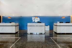 A hotel reception area with three reception desks, a blue wall, and overhead lighting. - Holiday Inn Express Shanghai Chongming by IHG (Shanghai)