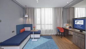 Habitació d'hotel moderna amb sofà llit, taula petita, televisió i zona de treball.