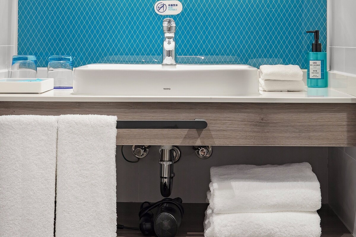 A bathroom with a white sink, blue tiled backsplash, a mirror, and a towel rack.