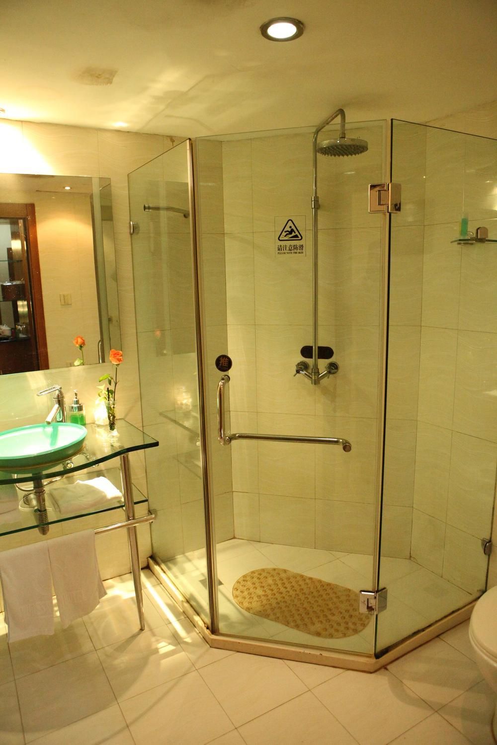 A glass-enclosed shower with a handheld showerhead, a glass sink with a towel, and a toilet.