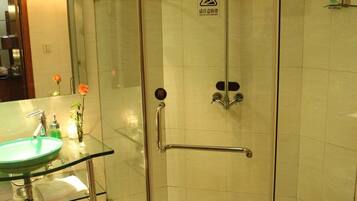 A glass-enclosed shower with a handheld showerhead, a glass sink with a towel, and a toilet.