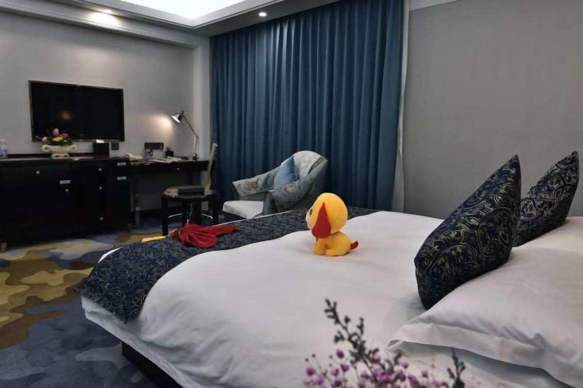 A hotel room with a bed, a desk, a chair, a television, and a large window with curtains.