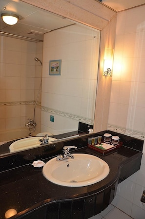 A bathroom with a large mirror, a sink, a shower, and a vanity with toiletries. - University Academic Exchange Hotel - Qingdao (Qingdao)