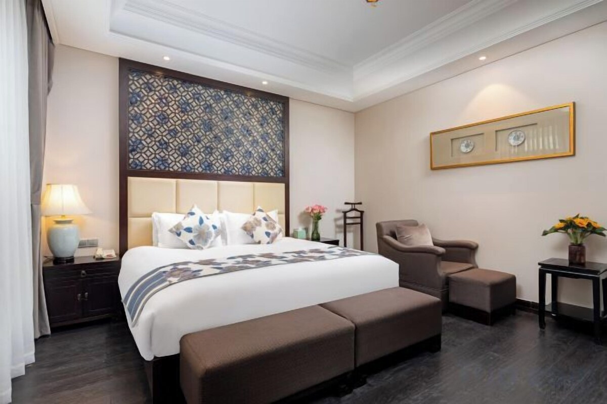 Een hotelkamer met een groot bed, een stoel, een klein tafeltje en een decoratief wandpaneel.
