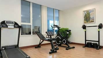 Un gimnasio con cinta de correr, bicicletas estáticas y una estructura para sentadillas.