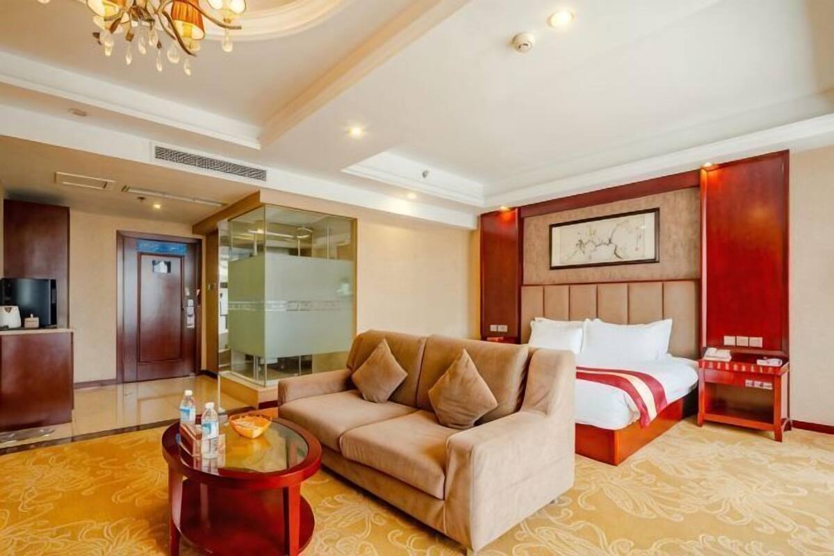 Habitación de hotel con sofá, cama, una mesita, una mesilla de noche y una obra de arte colgada en la pared.