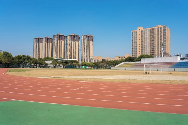 A running track with a green field and a tall building in the background.