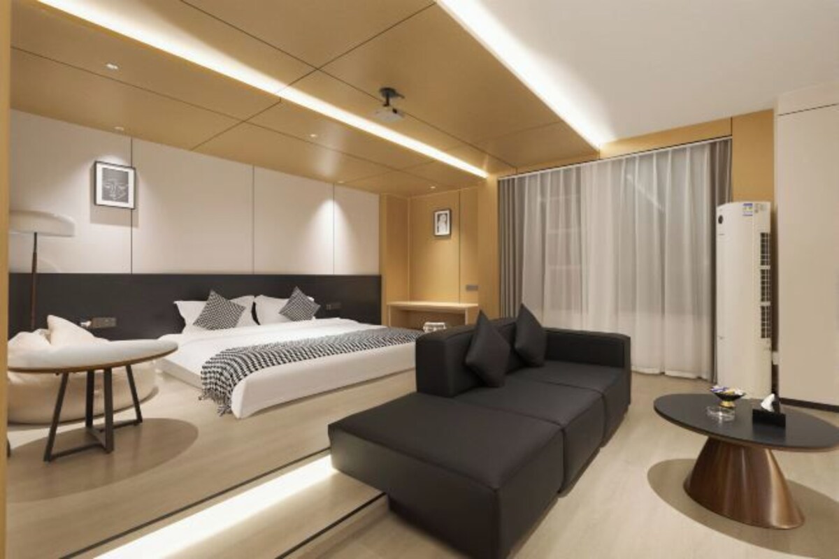 A modern hotel room with a bed, a sofa, a round table, and a flat-screen TV.