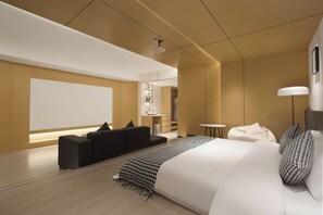 A modern hotel room with a large bed, a seating area, a small table, and a lamp.