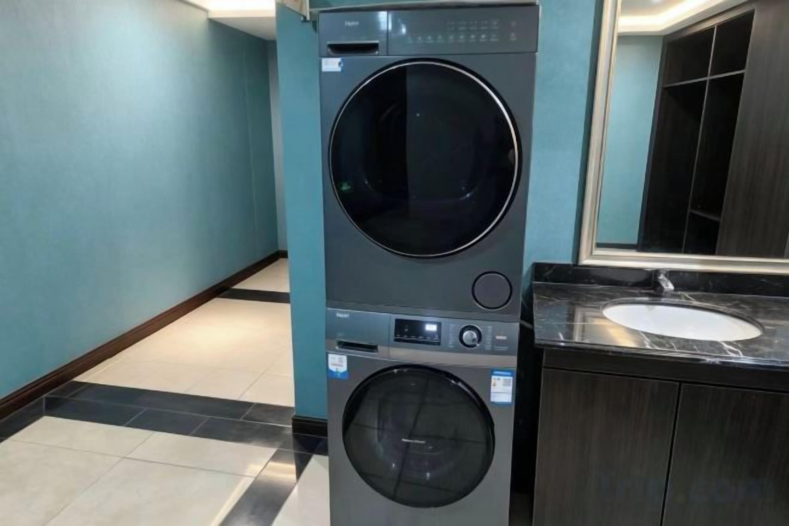 A compact washer and dryer unit in a modern bathroom with a sink and mirror.