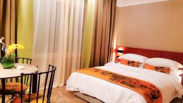 A hotel room with a bed, a dining table with chairs, and a vase with flowers.