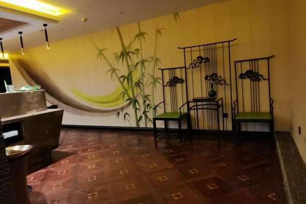 Una habitación con un mural de bambú, una recepción de madera y dos sillas verdes.